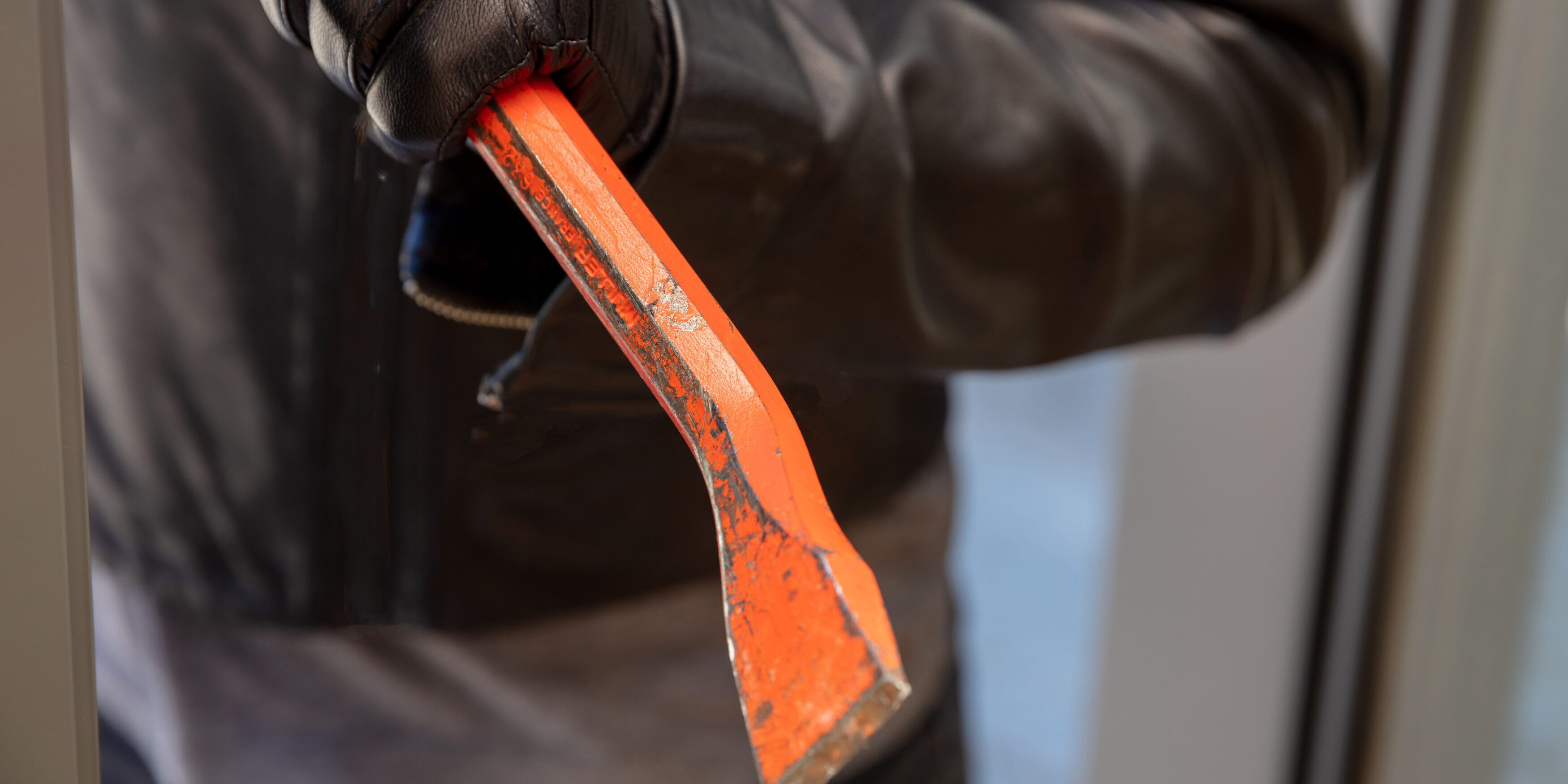 Thief holding a crowbar to break a glass window.