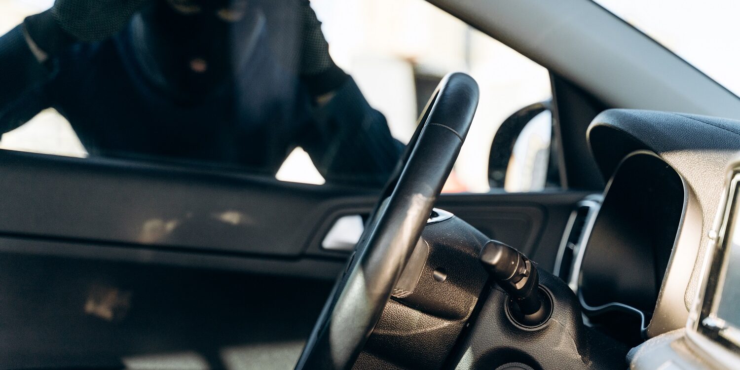 View from the car at the man dressed in black with a balaclava on his head looking at the glass of car before the stealing. Car thief, car theft concept