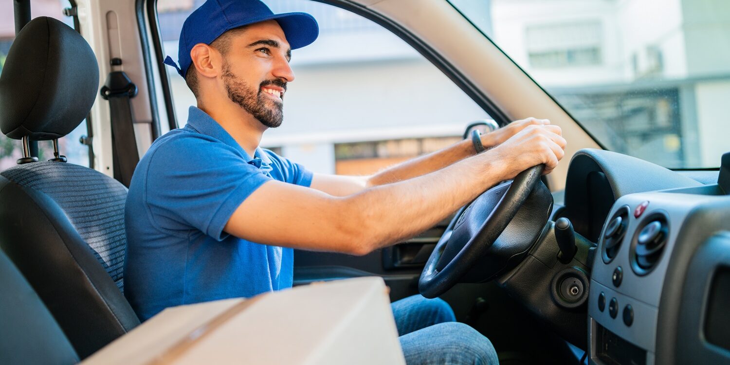 Delivery man driving van with cardboard boxes on seat.