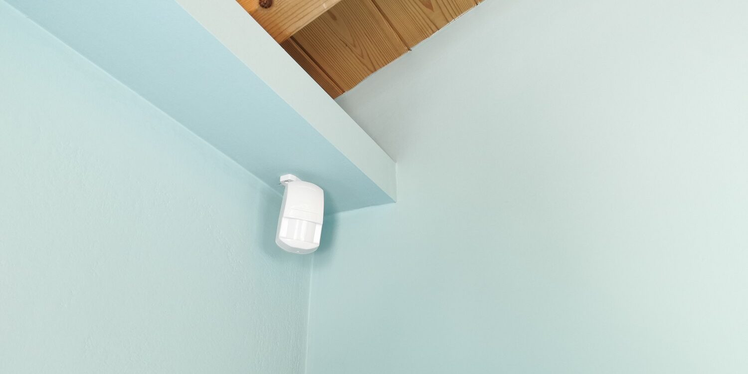 Motion sensor or detector for security system mounted on blue wall in mansard room with wooden ceiling