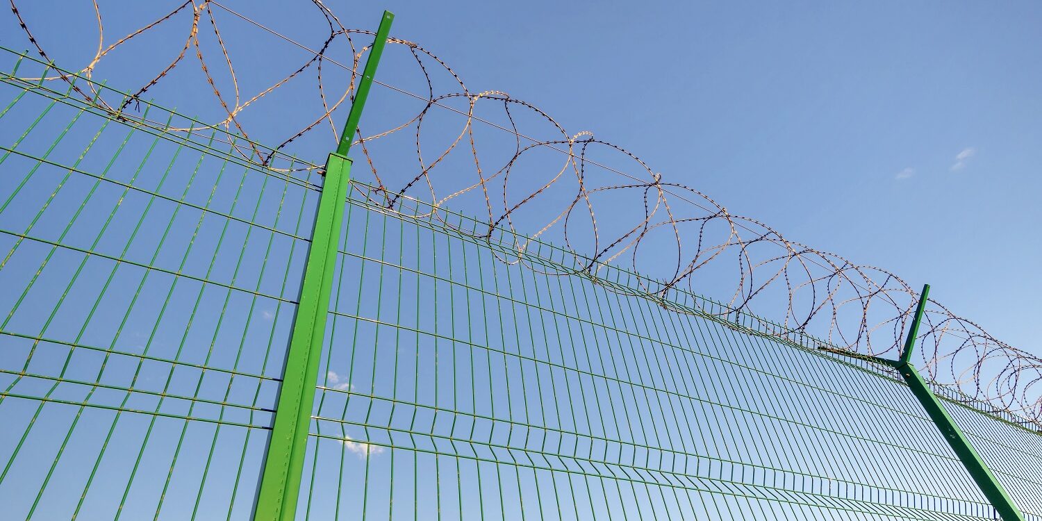 Slatted fence with barbed wire on top.