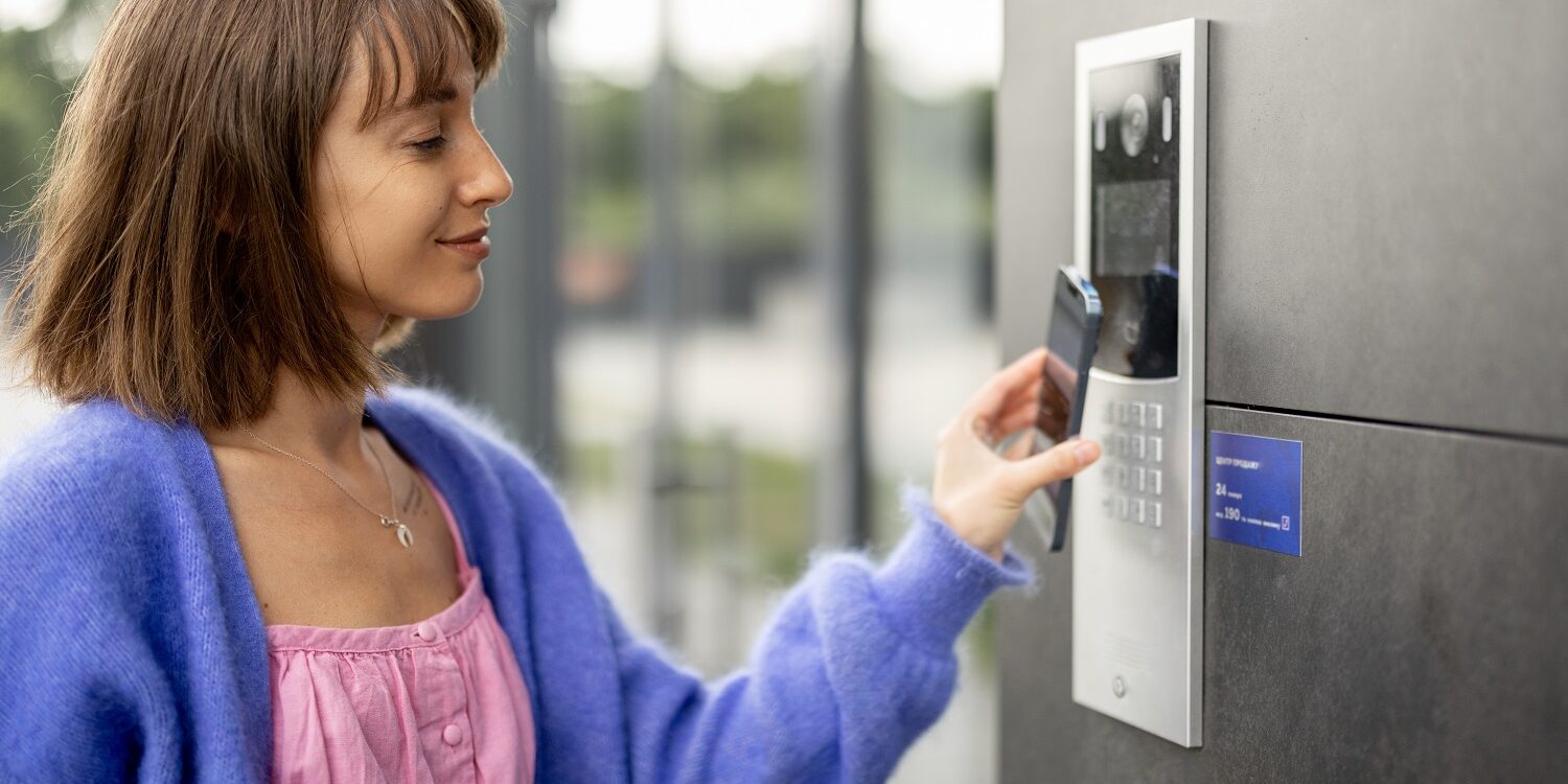 Young stylish woman getting access to the building by attaching smartphone to intercom