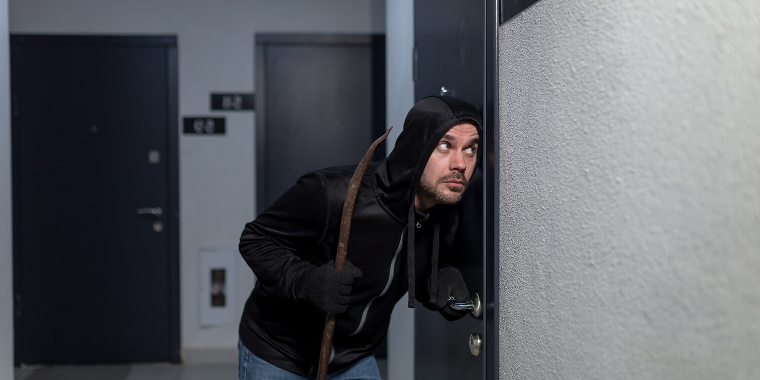 The robber tries to break the door lock in the apartment, dressed in black