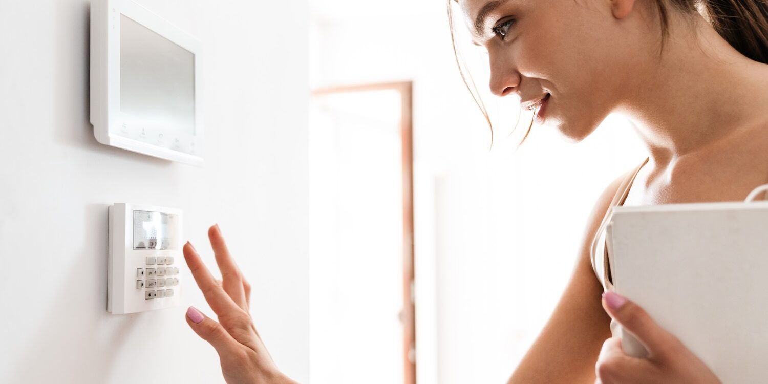 Young woman entering code on keypad of home security alarm